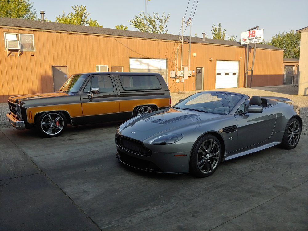 Aston Martin convertible and classic Chevy SUV detailed to a high gloss outside the shop